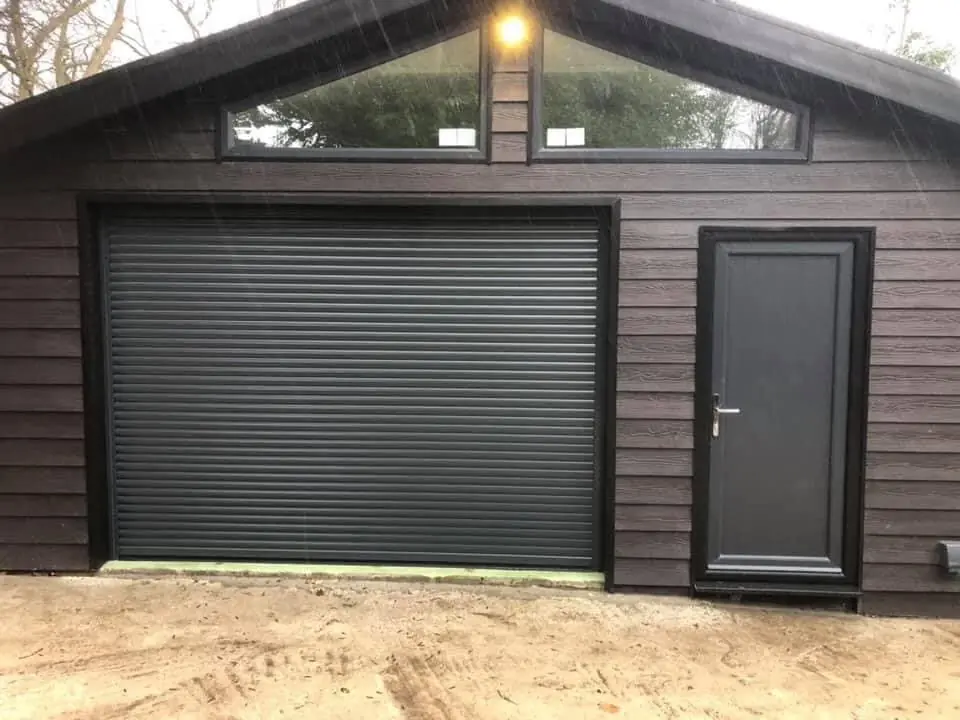 Anthracite roller garage door and matching side door on a dark timber-clad garage