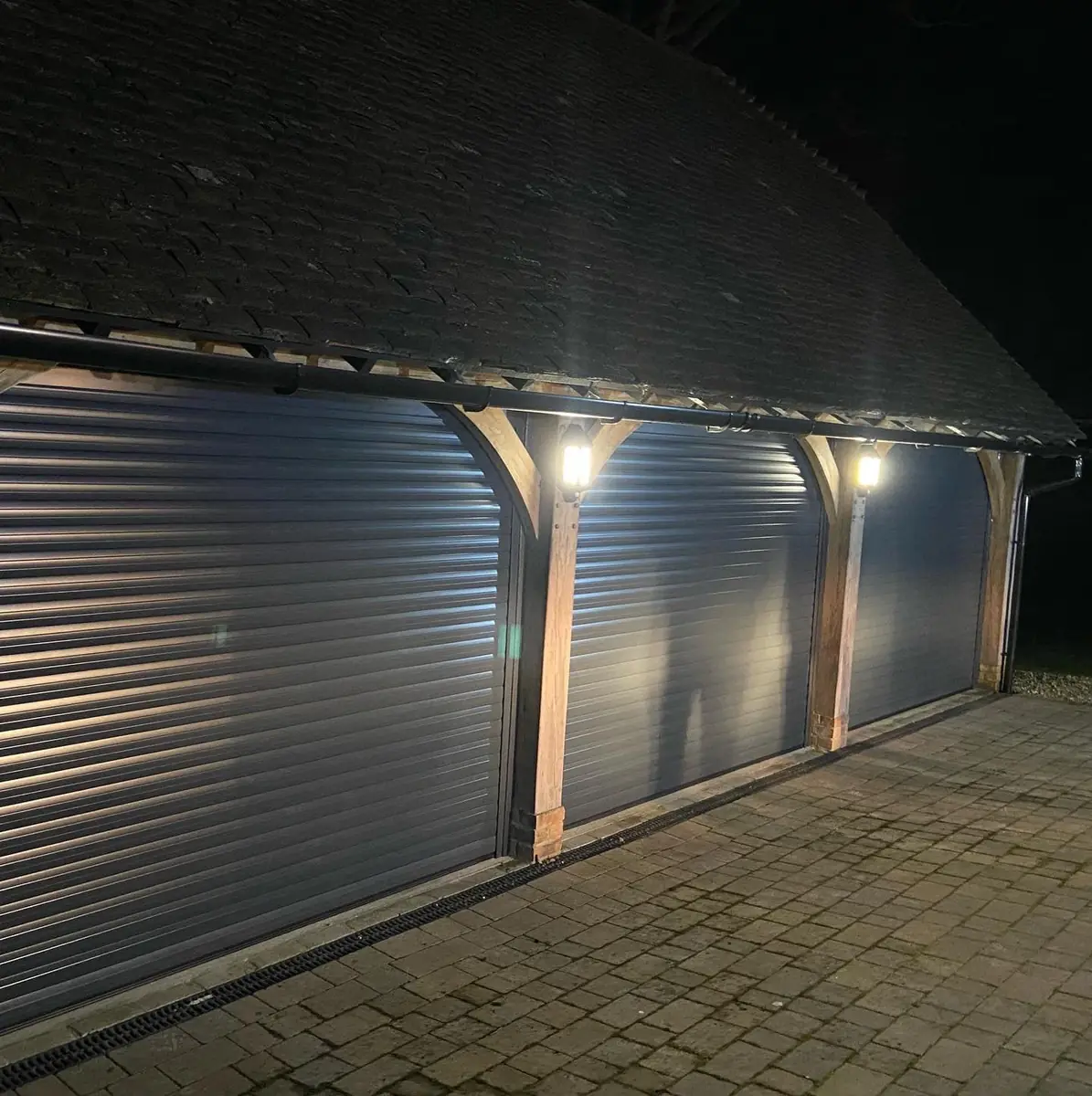 Anthracite roller garage doors lit up at night in an oak-framed garage