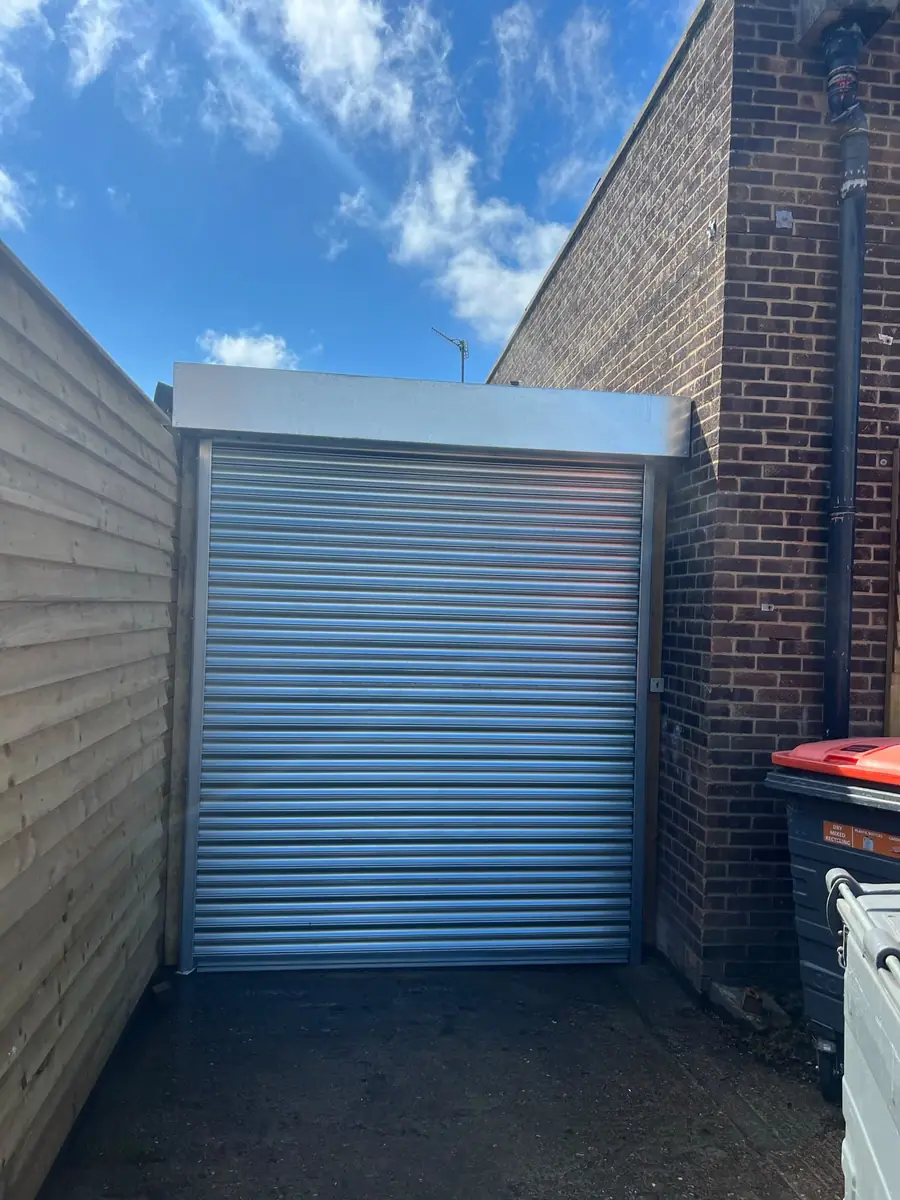 Galvanised roller shutter closing off a rear yard between a fence and a brick wall