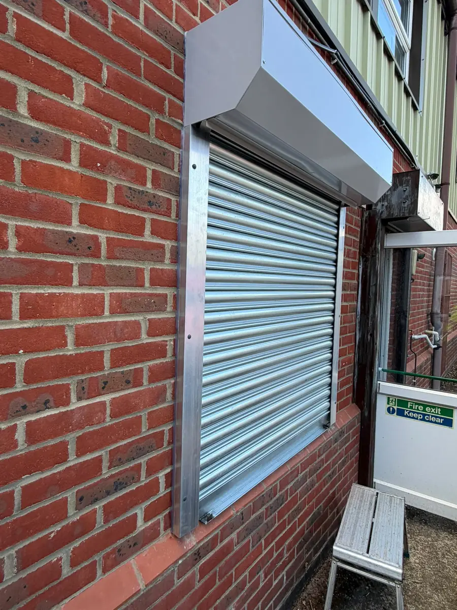 Galvanised steel roller shutter over a window on a commercial brick building