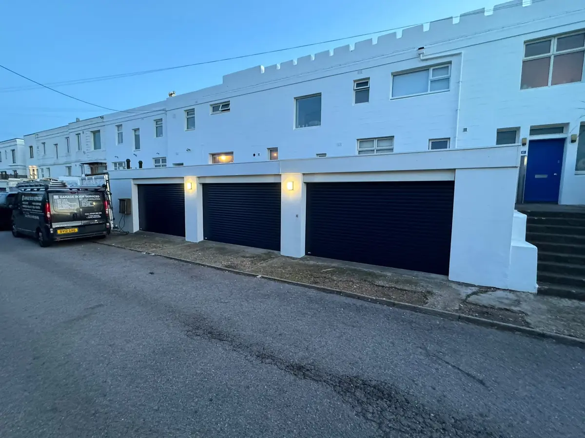 Three navy roller garage doors with wall lights beneath a white terrace