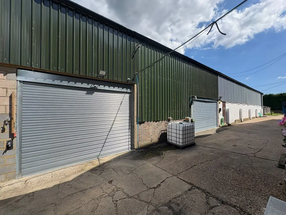 Galvanised roller shutters on a long green-clad warehouse