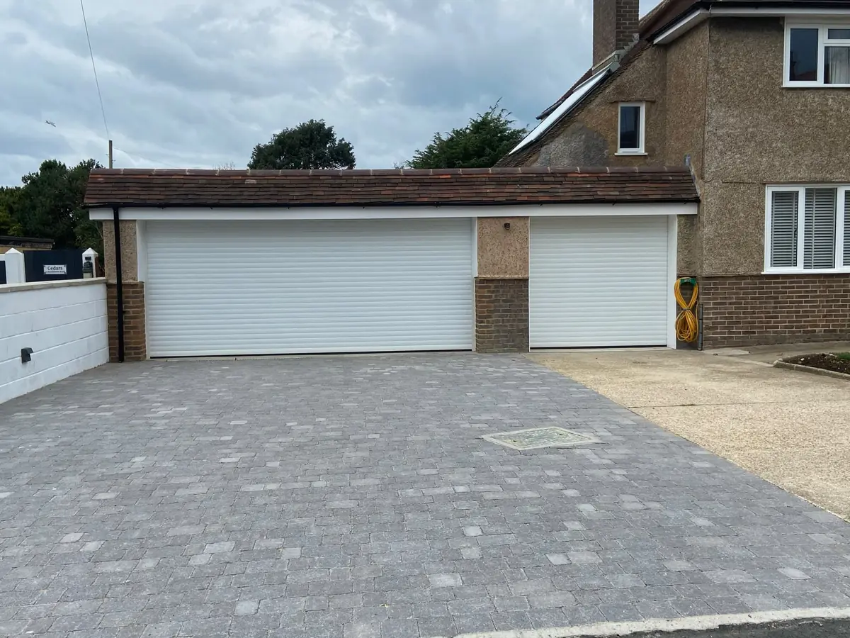 White roller garage doors on a wide double garage and a single garage beside a bungalow