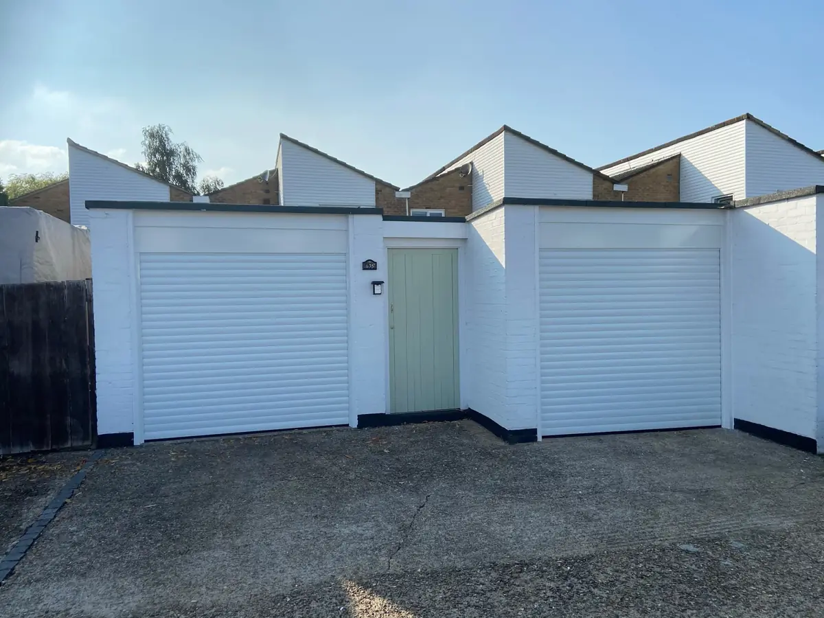 Two white roller garage doors either side of a sage green front door