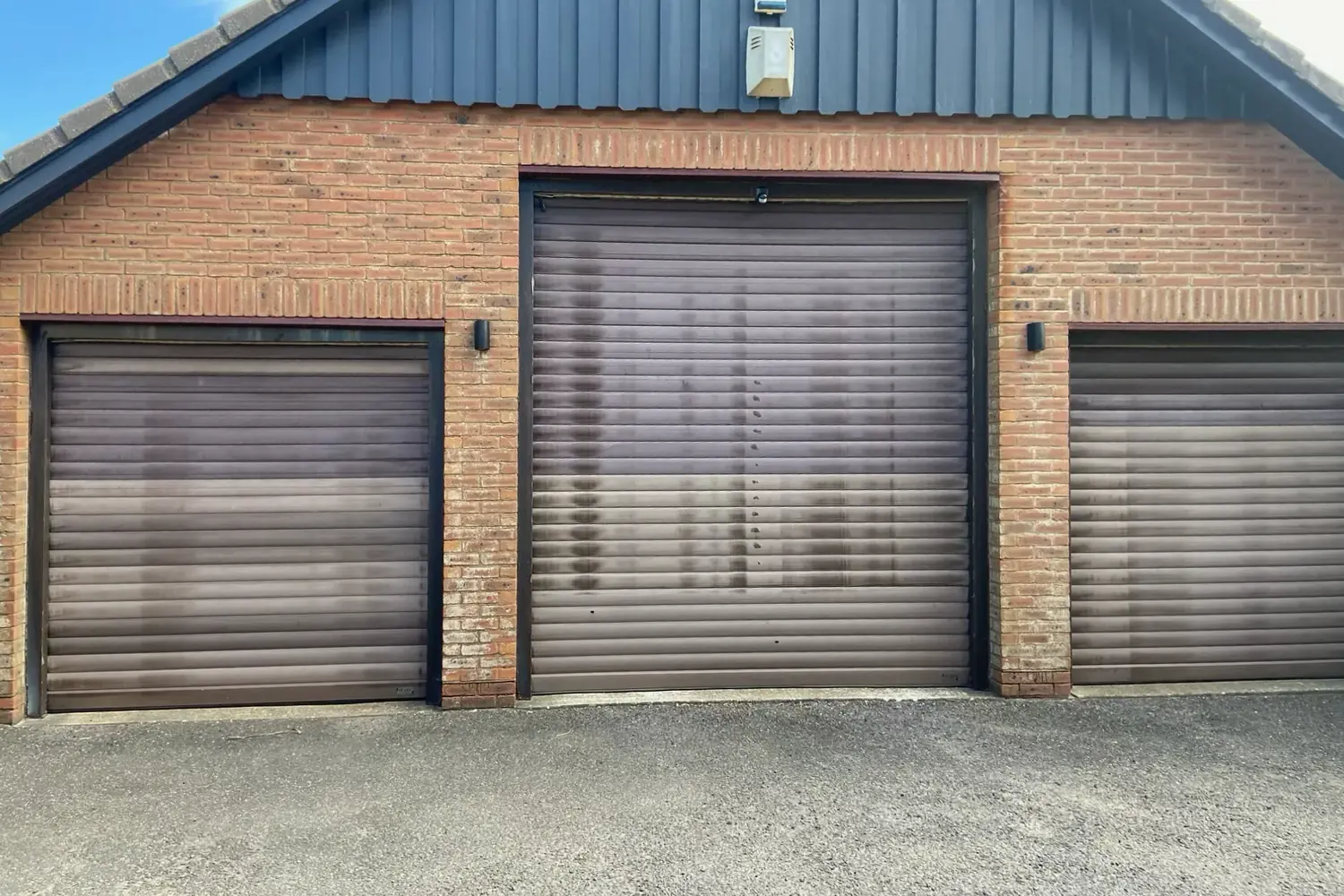 Three faded and water-stained brown roller doors on a brick triple garage